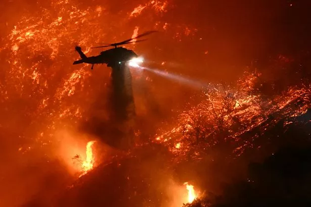 Um helicóptero de combate a incêndio joga água enquanto o incêndio em Palisades cresce perto do Mandeville Canyon